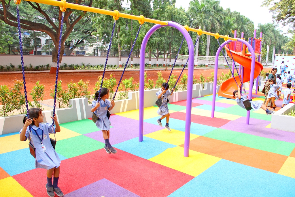 A Pretty Cheerful Little Kids are having fun on a Swing in a School Playground.